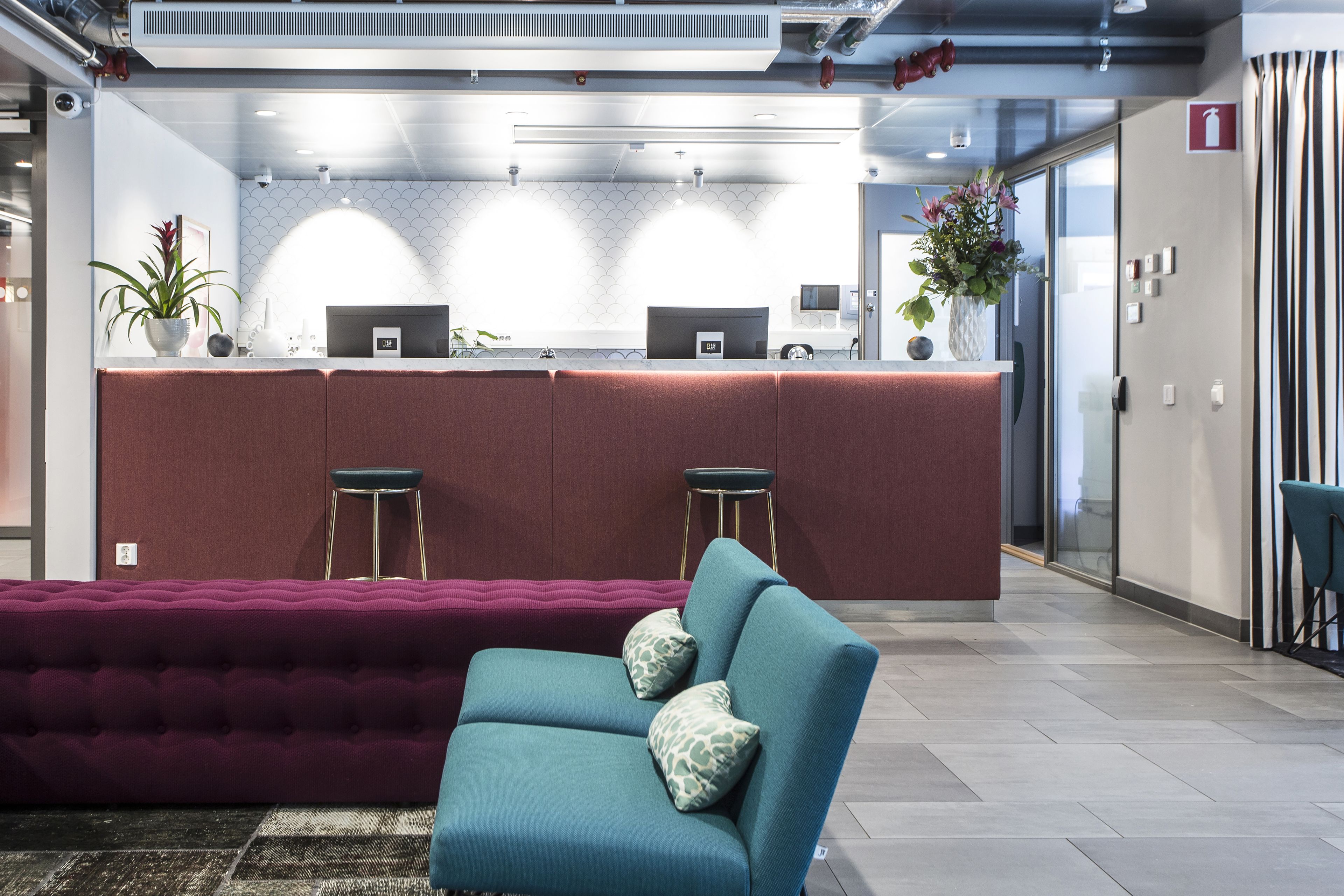 Un espace d’accueil moderne avec un canapé turquoise, un banc rembourré rouge et un comptoir de bar agrémenté de deux tabourets.