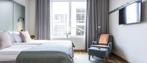 A modern bedroom with a large bed, a chair, a TV, and a window with curtains.