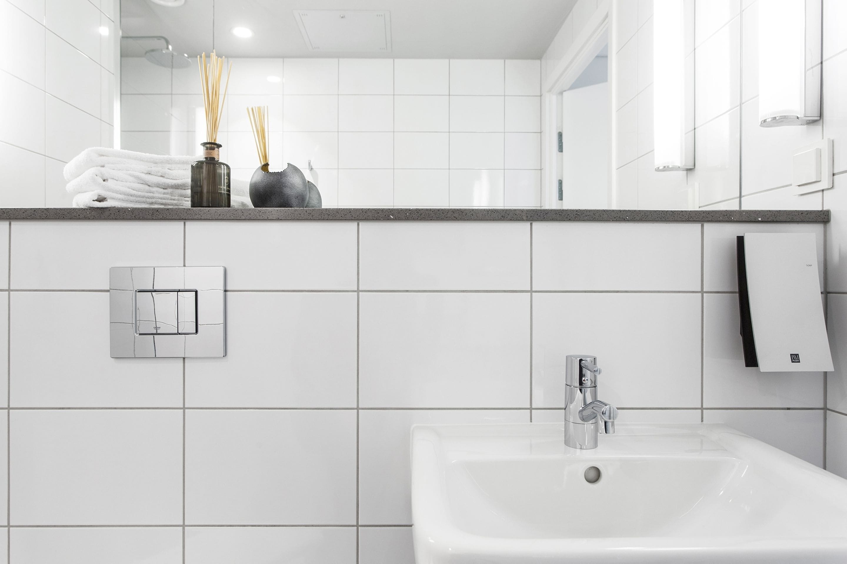 Een moderne badkamer met witte tegels, een wastafel, een handdoekdispenser en een spiegel.