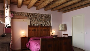 A bedroom with a wooden bed, stone wall, wooden ceiling beams, and a white door. - Relais Corte Sant'Agata (Verona)