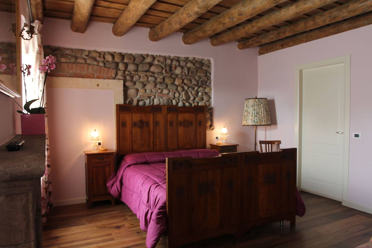 A bedroom with a wooden bed, stone wall, wooden ceiling beams, and a white door.