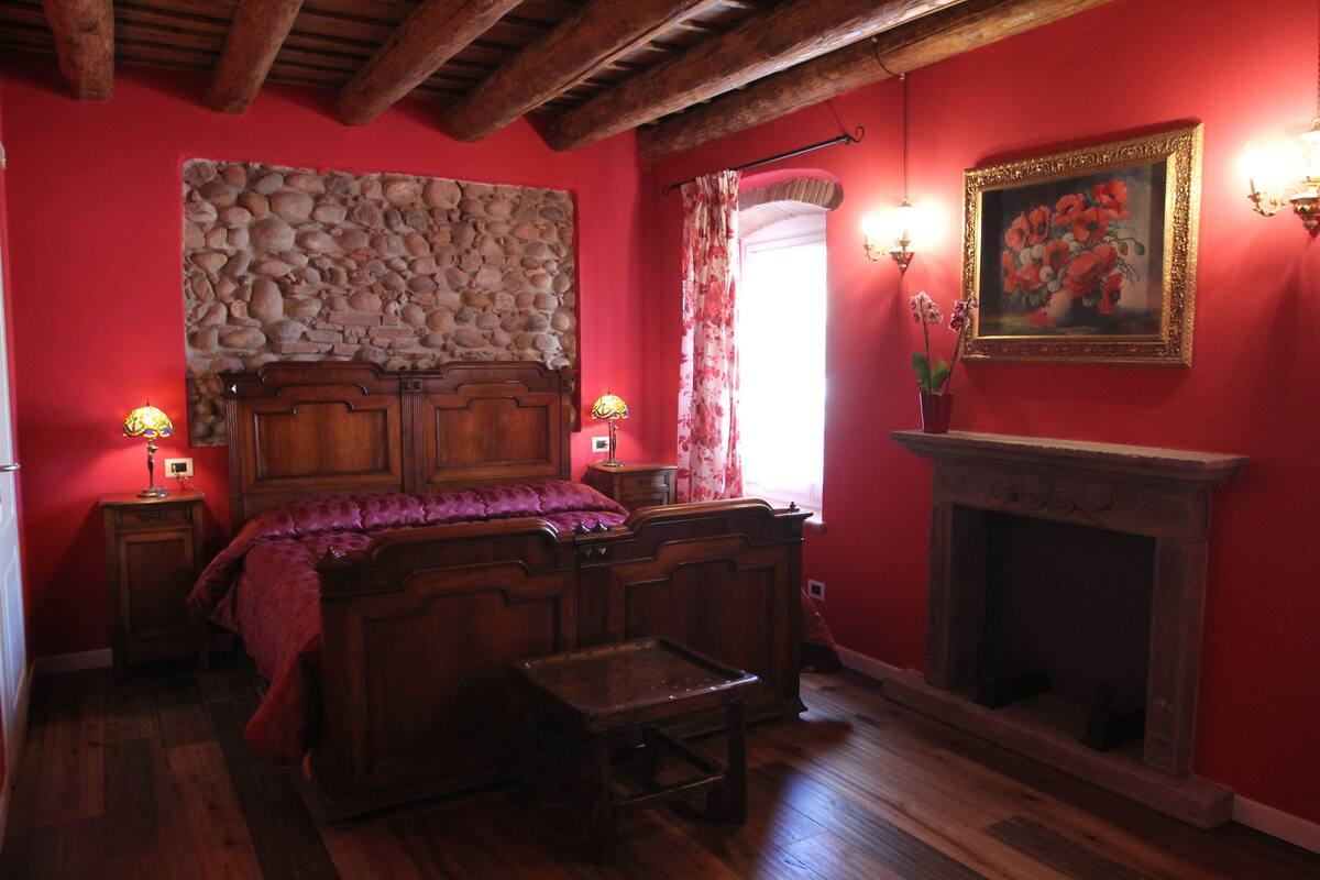 A room with a stone wall, wooden bed, fireplace, and two wall-mounted lamps.