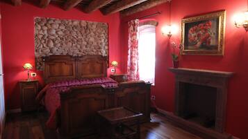 A room with a stone wall, wooden bed, fireplace, and two wall-mounted lamps.