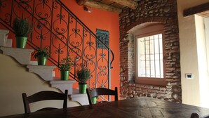 A dining area with a wooden table and chairs, a staircase with decorative railing, and a stone wall with a window. - Relais Corte Sant'Agata (Verona)