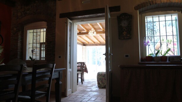 A dining area with a table and chairs, a kitchen area with a window and potted plants, and a hallway leading to another room. - Relais Corte Sant'Agata (Verona)