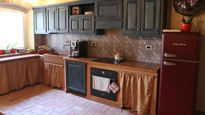 A kitchen with wooden cabinets, a red refrigerator, and a tiled backsplash. - Relais Corte Sant'Agata (Verona)