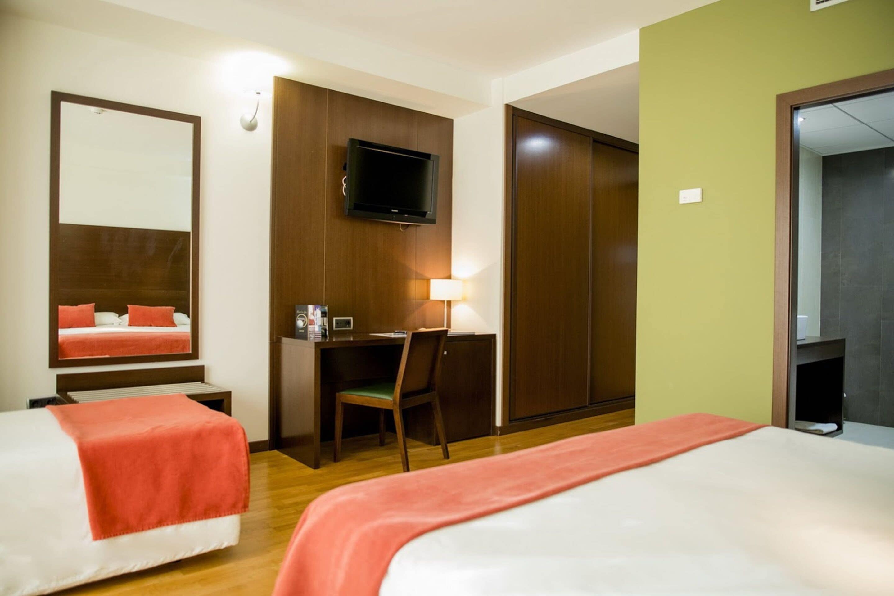 Habitación de hotel con dos camas, un escritorio con silla, un televisor y un armario.