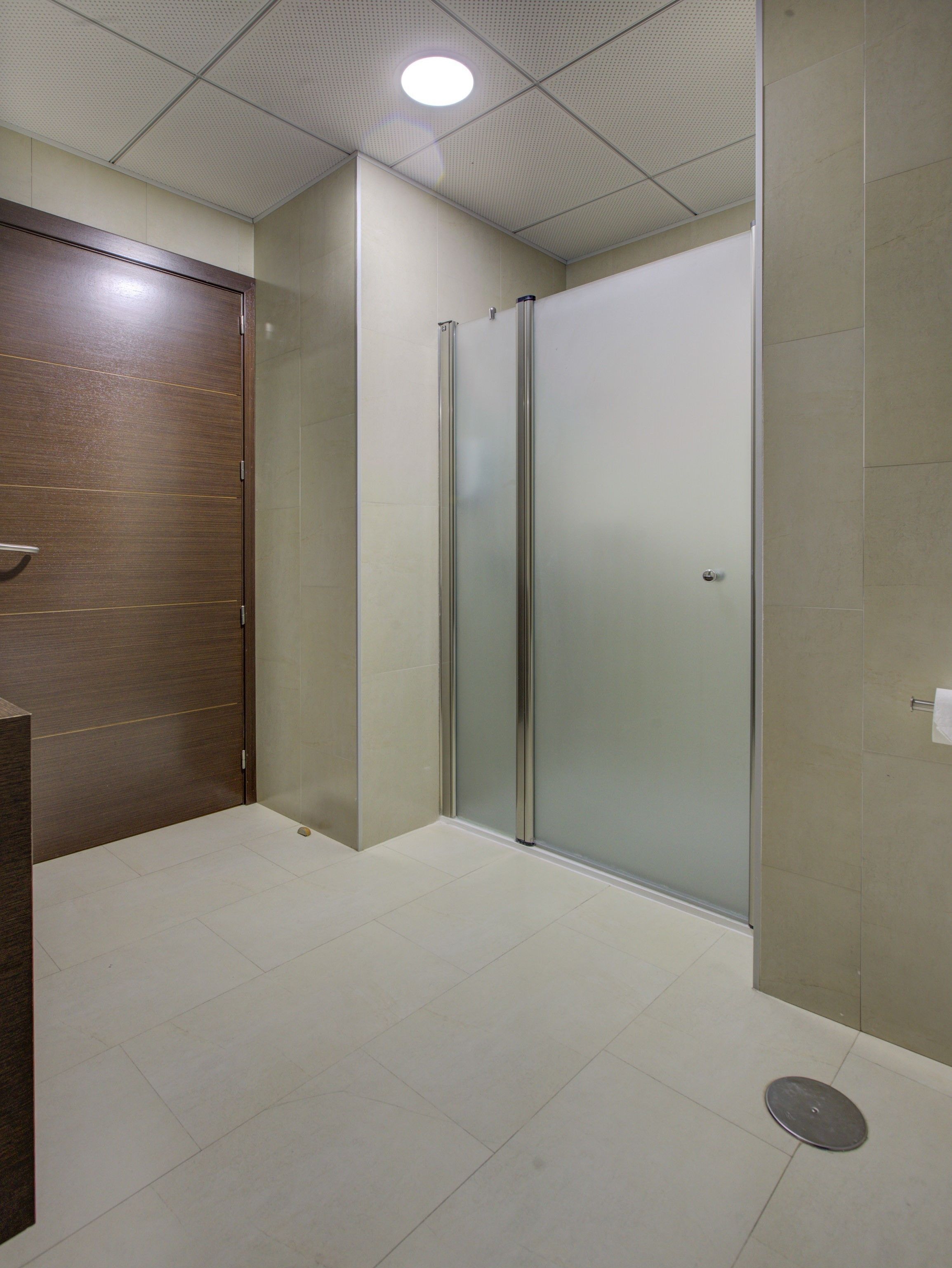 Un baño moderno con puerta de madera, cabina de ducha de vidrio y suelo de baldosas.