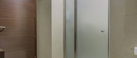 A modern bathroom with a wooden door, a glass shower enclosure, and a tiled floor.