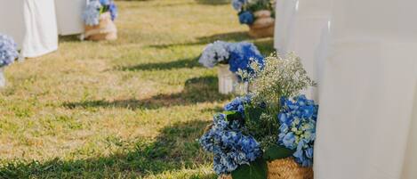 Un pasillo nupcial con sillas blancas y una cesta de mimbre con flores azules.