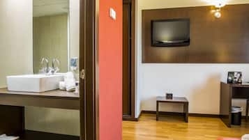 Ein Hotelzimmer mit einem großen Spiegel, einem weißen Waschbecken, Holzboden, einem kleinen Tisch, einem an der Wand montierten Fernseher und einer roten Akzentwand.