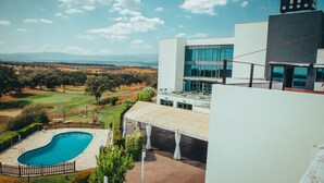 Un hotel moderno con piscina, vistas al campo de golf y un gran edificio con el letrero 'H'.