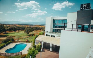 Un hotel moderno con piscina, vistas al campo de golf y un gran edificio con el letrero 'H'.