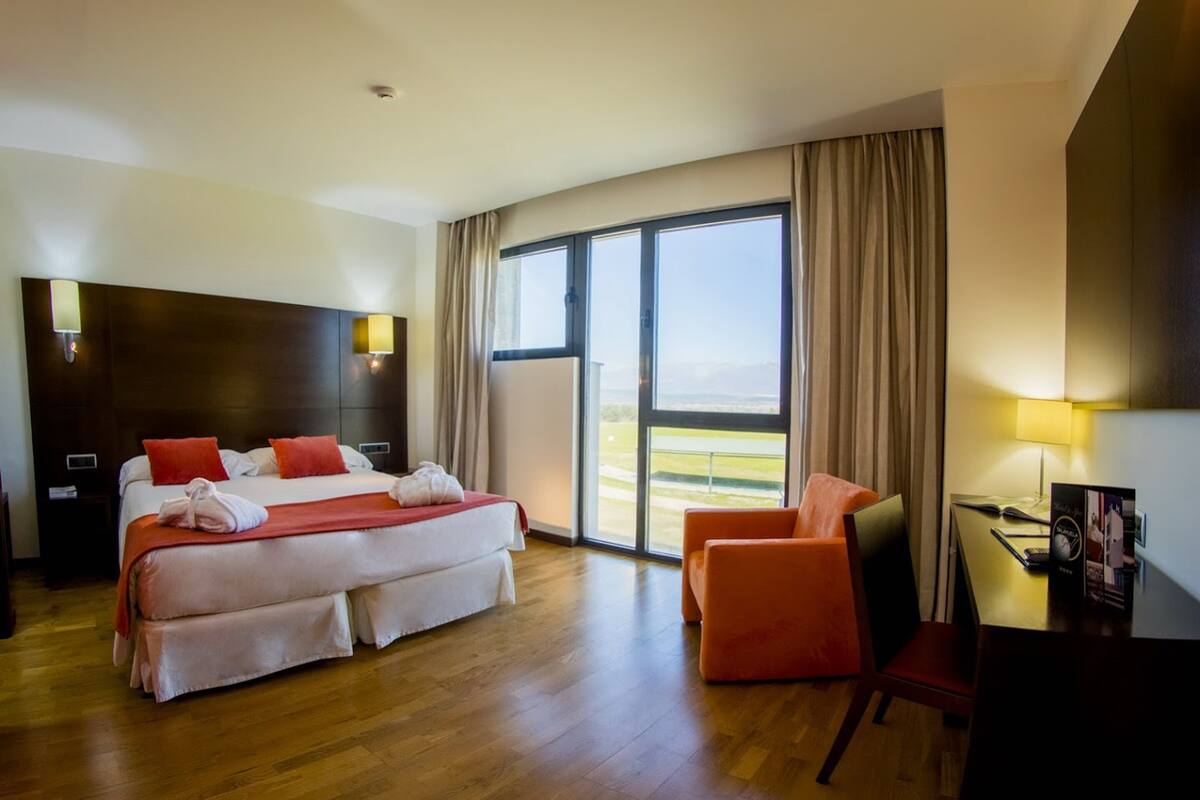 Een hotelkamer met een groot bed, een bureau, een stoel en uitzicht op een golfbaan door het raam.