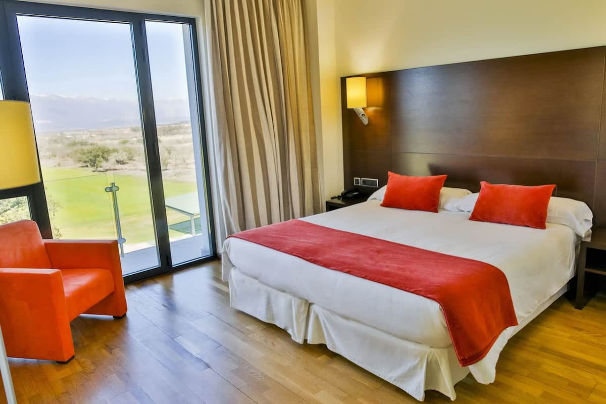 Hotelkamer met een groot bed, een stoel, een nachtkastje en uitzicht op een golfbaan door het raam.