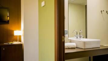 A hotel bathroom with a sink, mirror, and a wooden cabinet with a lamp.