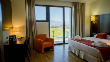 Habitación de hotel con cama, escritorio, silla y un ventanal con vistas a un paisaje verde.