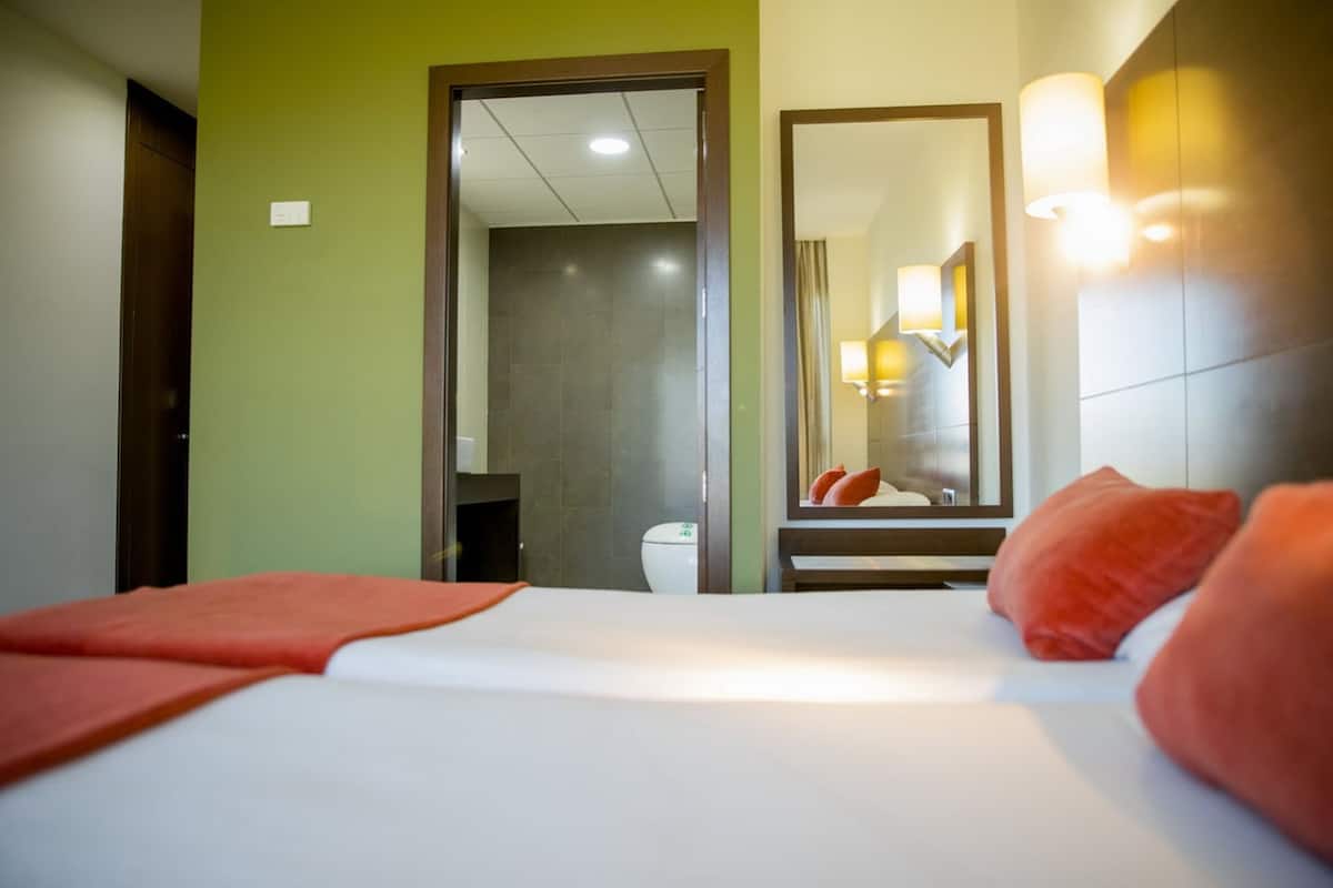 Een hotelkamer met een bed, een spiegel, een deur en een lamp.
