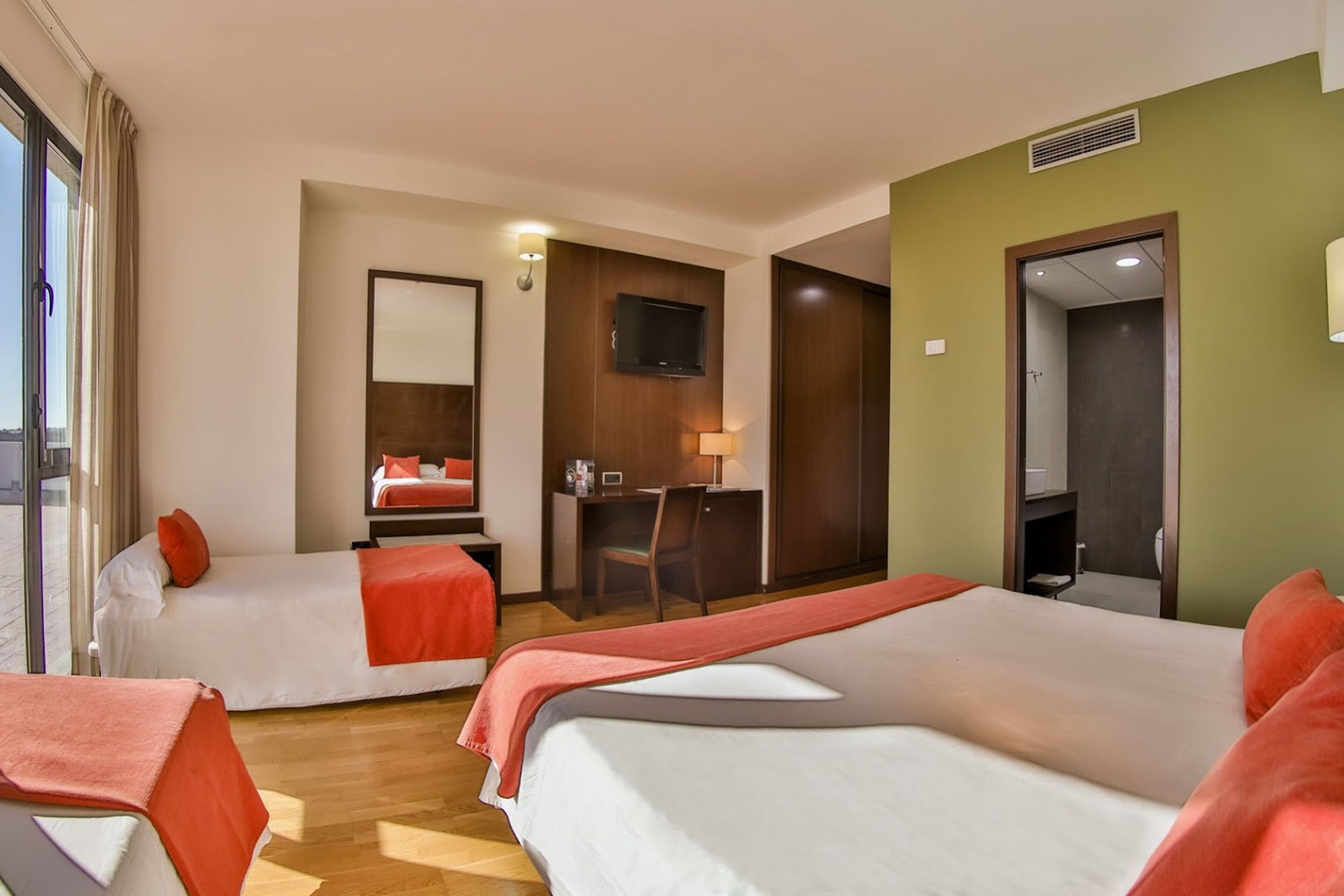 A hotel room with two beds, a desk, a TV, and a bathroom door.