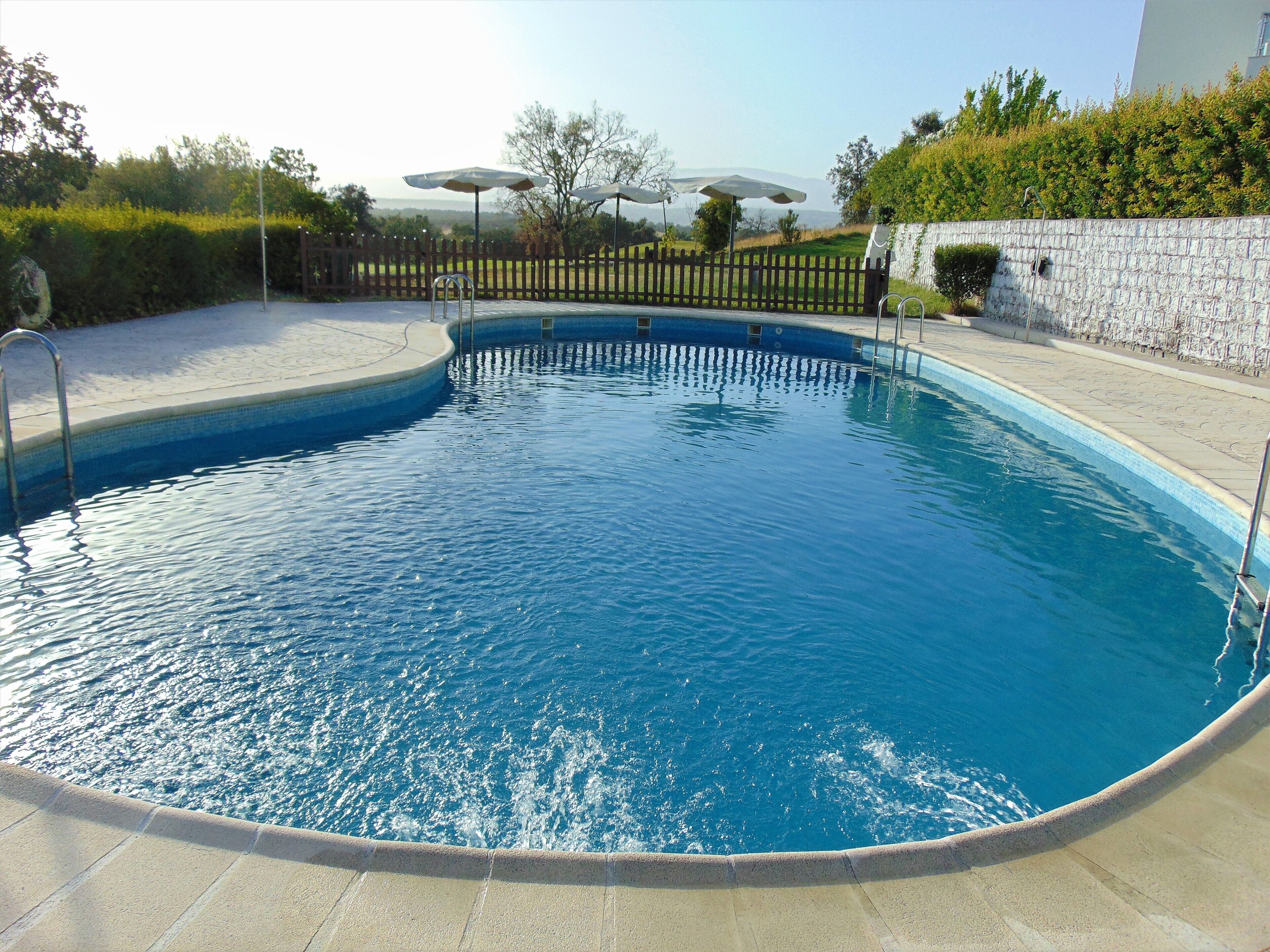 A swimming pool with a wooden fence, a stone wall, and umbrellas.