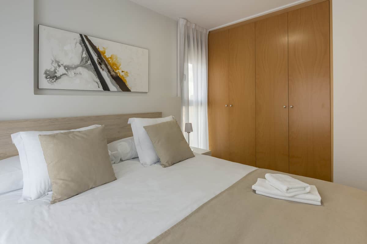 A hotel room with a bed, a wooden wardrobe, a painting on the wall, and a window with curtains.