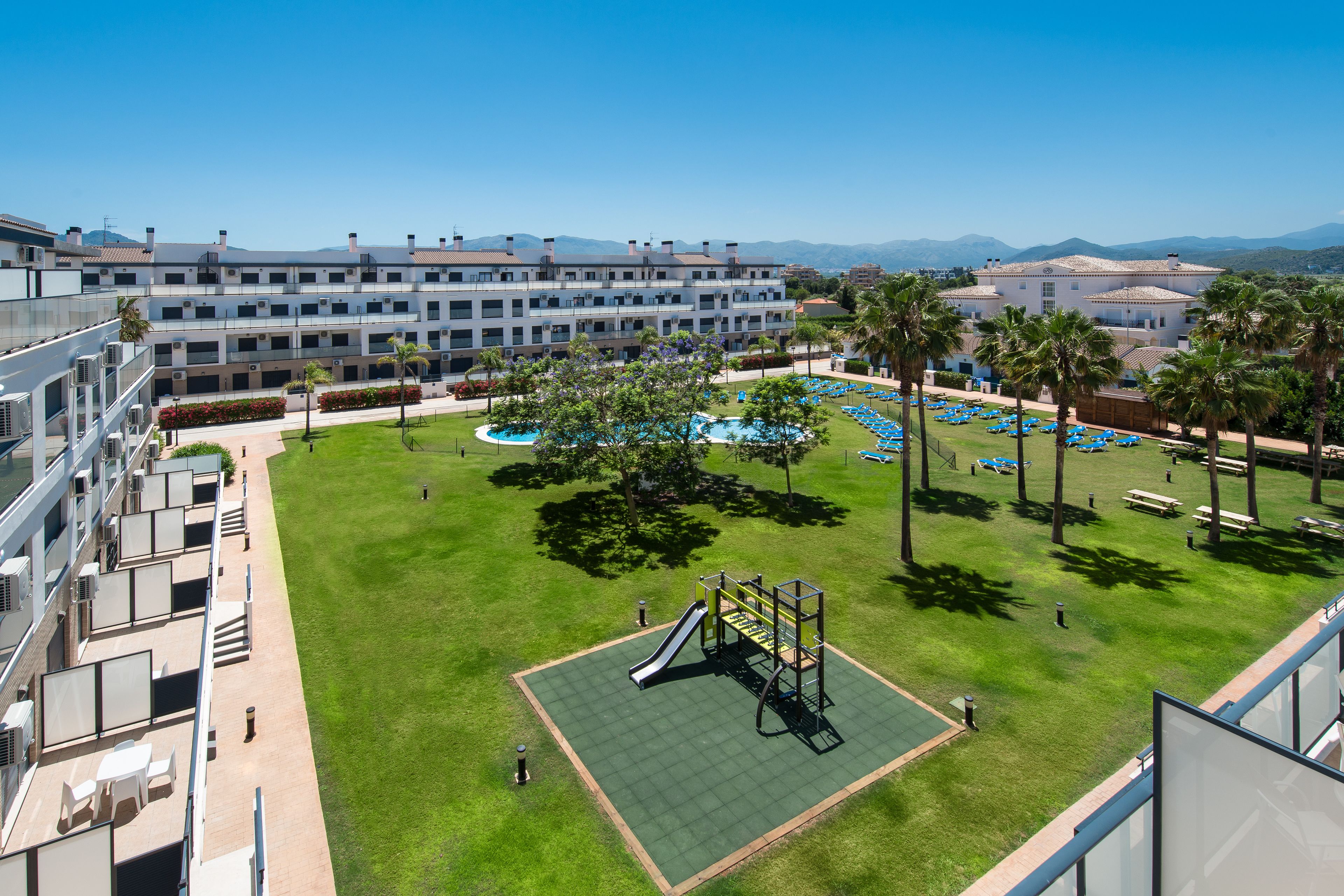 A hotel courtyard with a playground, palm trees, and a pool area.