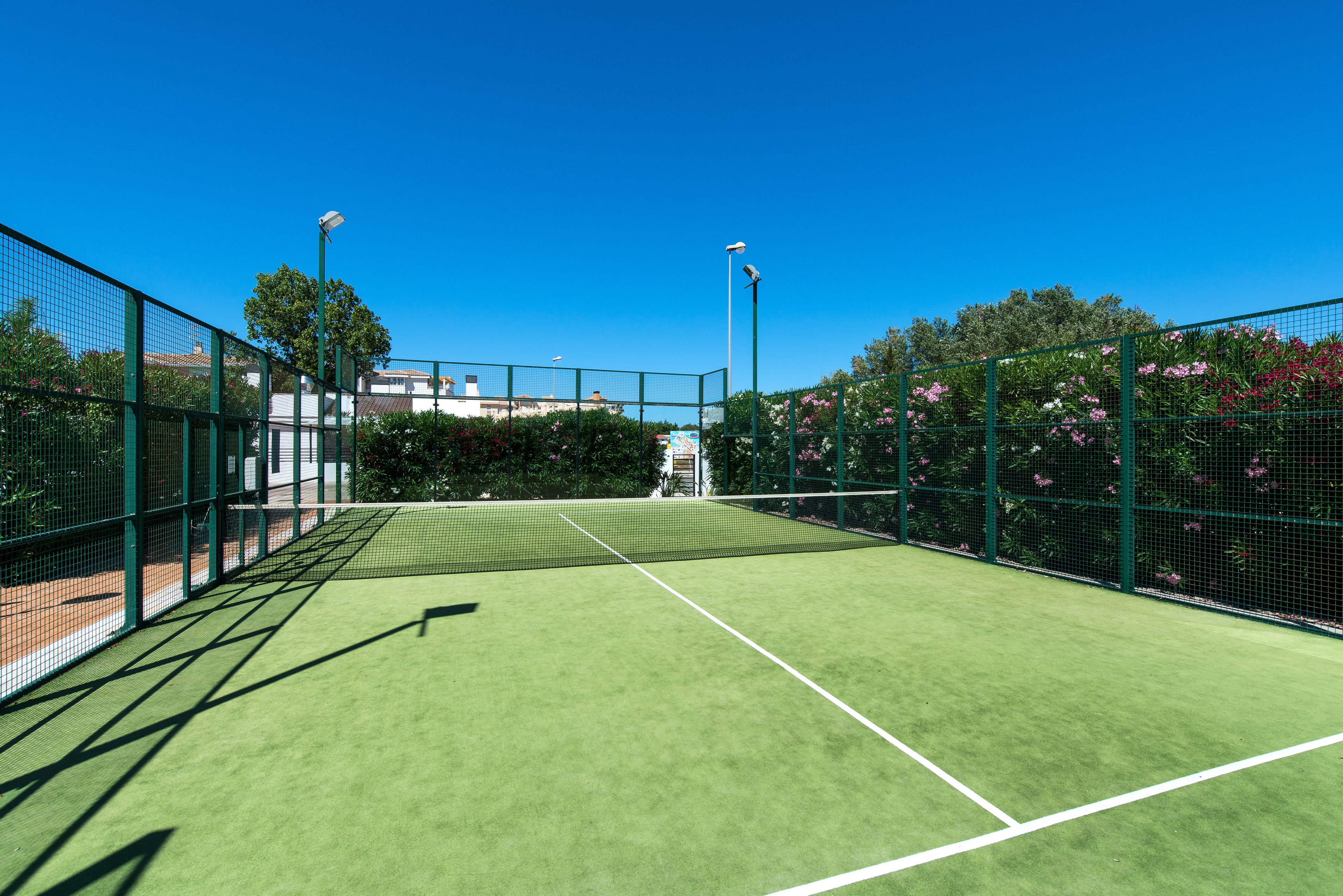 Una cancha de tenis con una red, rodeada de vallas verdes y árboles.