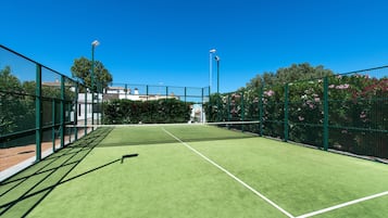 Una cancha de tenis con una red, rodeada de vallas verdes y árboles.