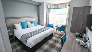 Ein Hotelzimmer mit Bett, Schreibtisch, Stuhl, Fernseher und einem Fenster mit Vorhängen.