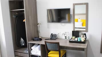 A hotel room with a desk, chair, TV, wardrobe, and a mirror.