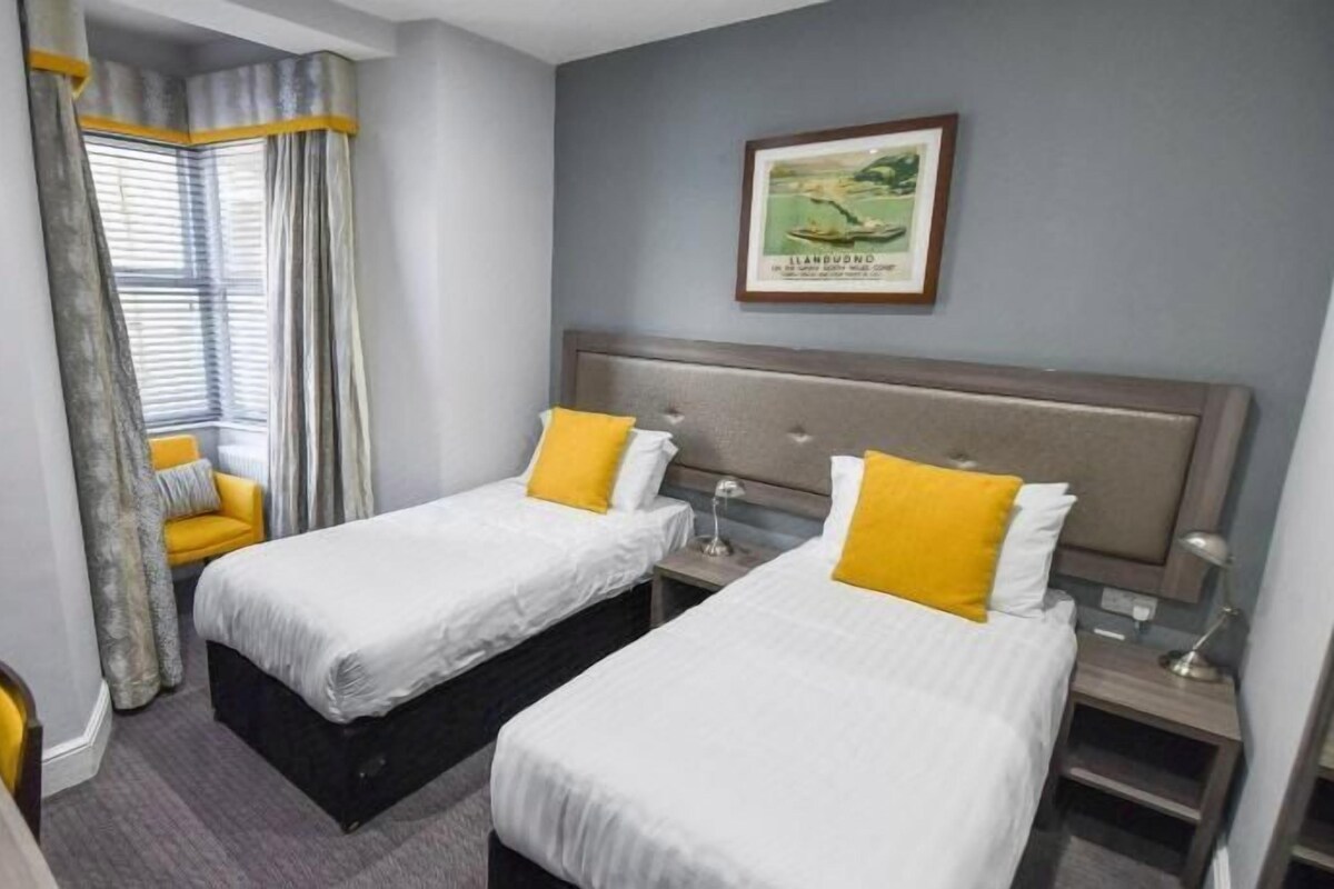 Habitación de hotel con dos camas, un escritorio y una ventana con cortinas.