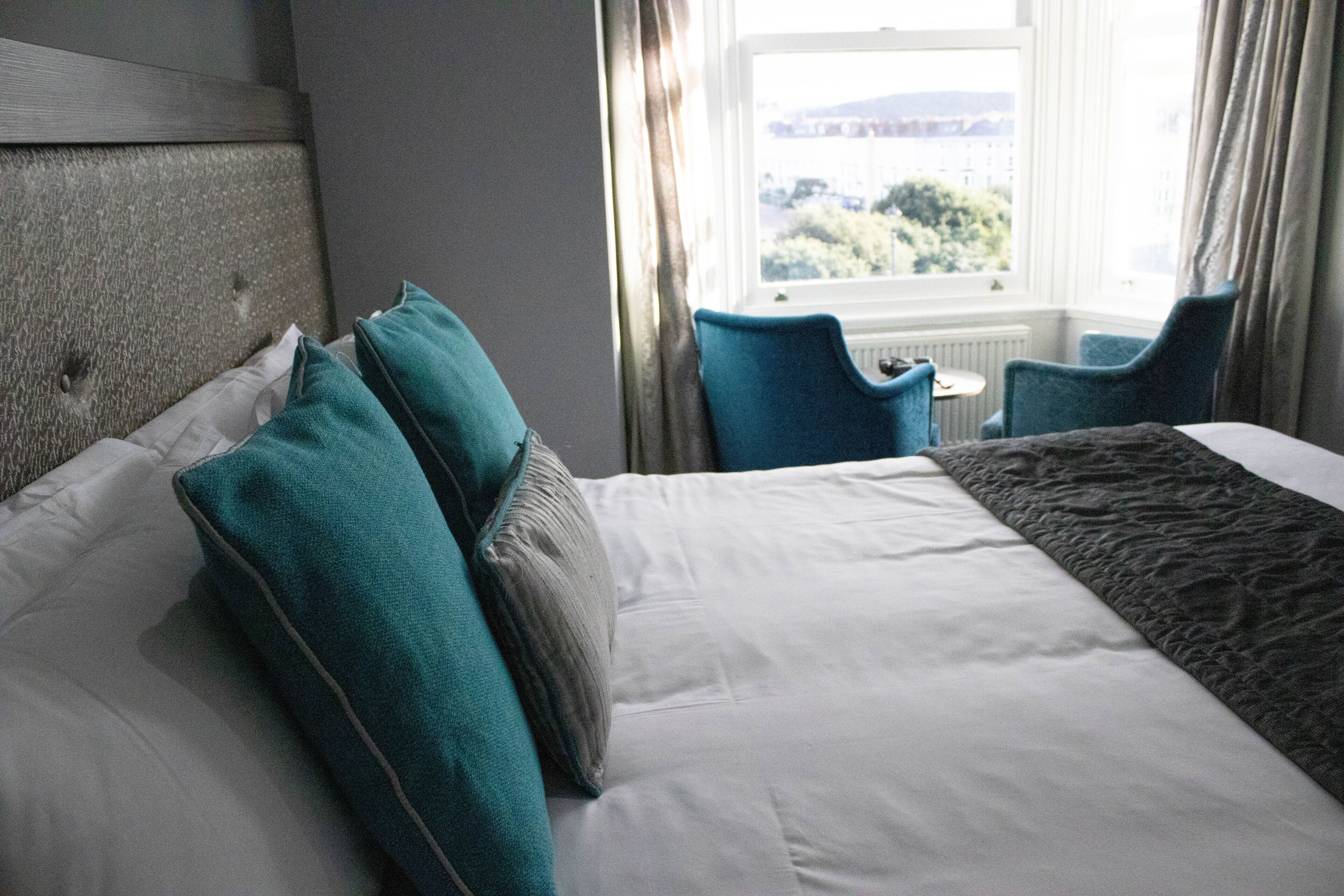 A hotel room with a large bed, two chairs, a small table, and a window with curtains.