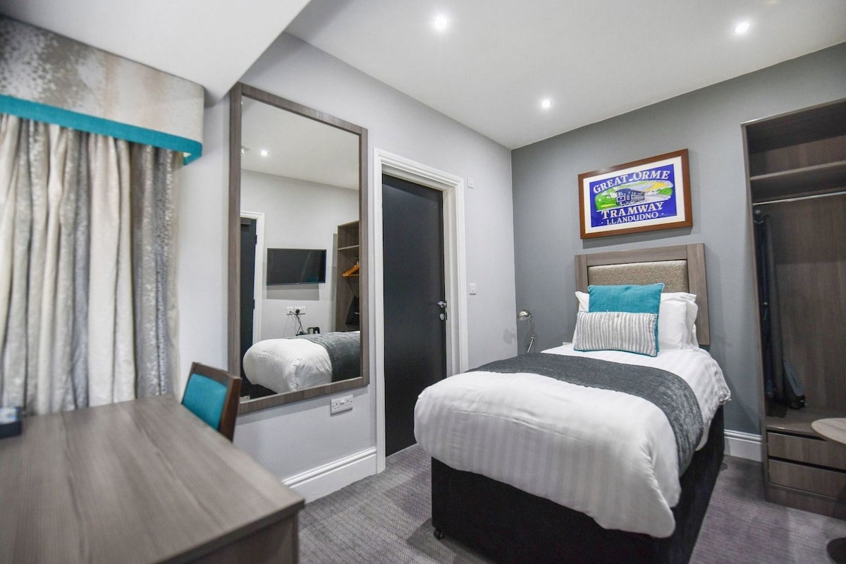 Una habitación de hotel con cama, escritorio, espejo, armario y un cartel enmarcado en la pared.