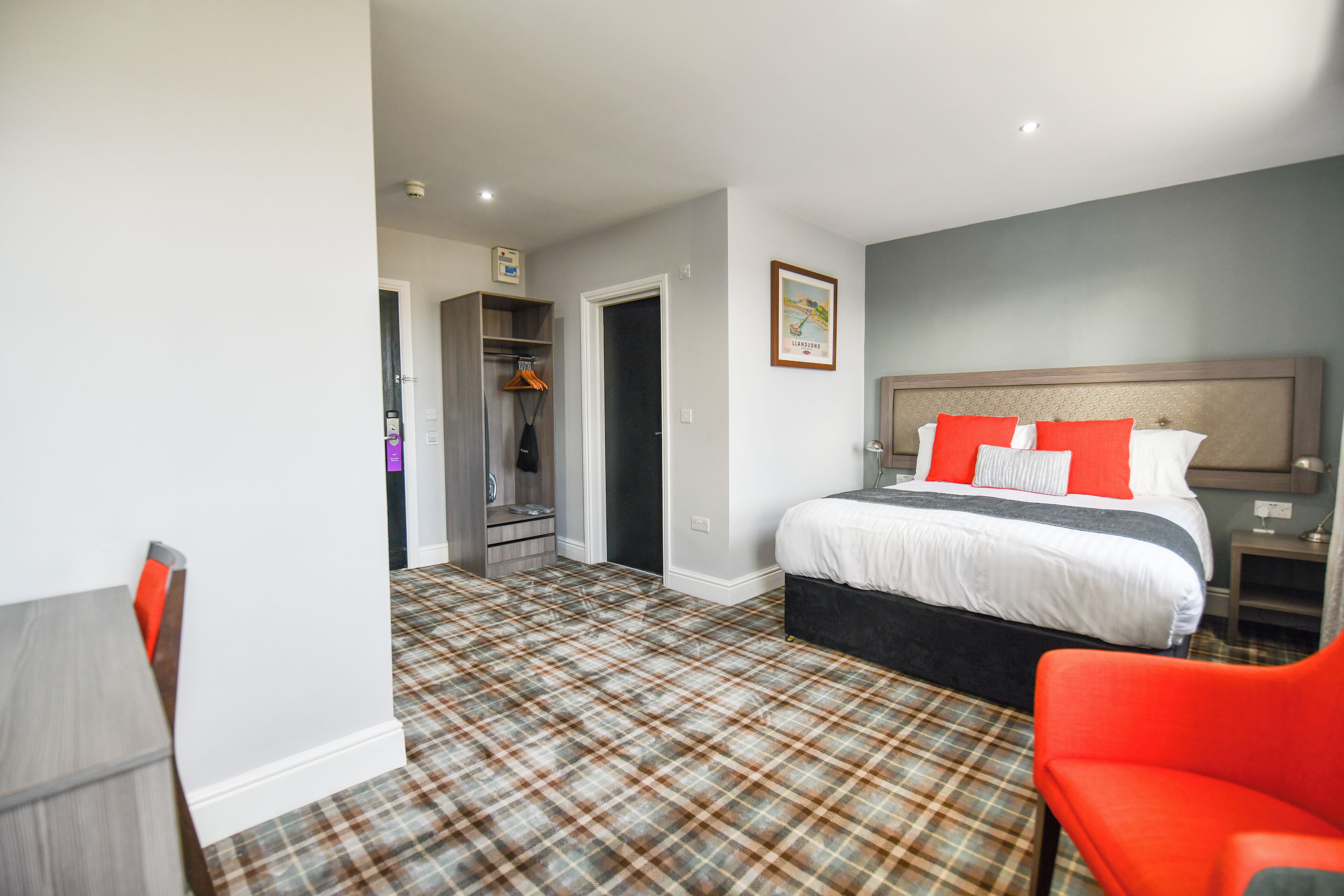 A hotel room with a bed, a red chair, a desk, and a wardrobe.