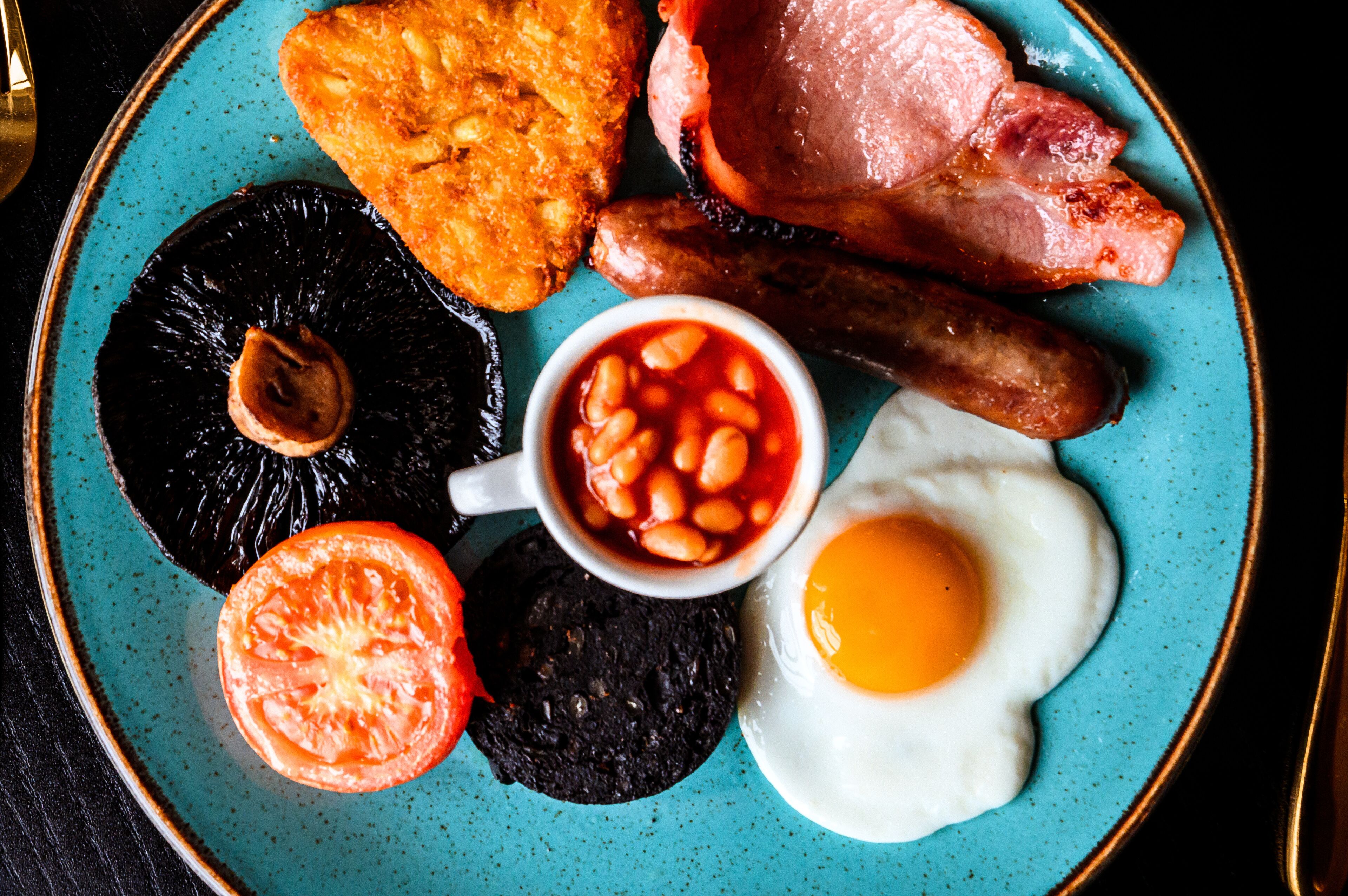 A plate with a variety of breakfast items including eggs, bacon, sausages, black pudding, baked beans, and a slice of tomato.