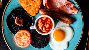 A plate with a variety of breakfast items including eggs, bacon, sausages, black pudding, baked beans, and a slice of tomato.