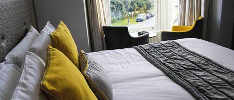 A hotel room with a bed, pillows, a window, and a chair.