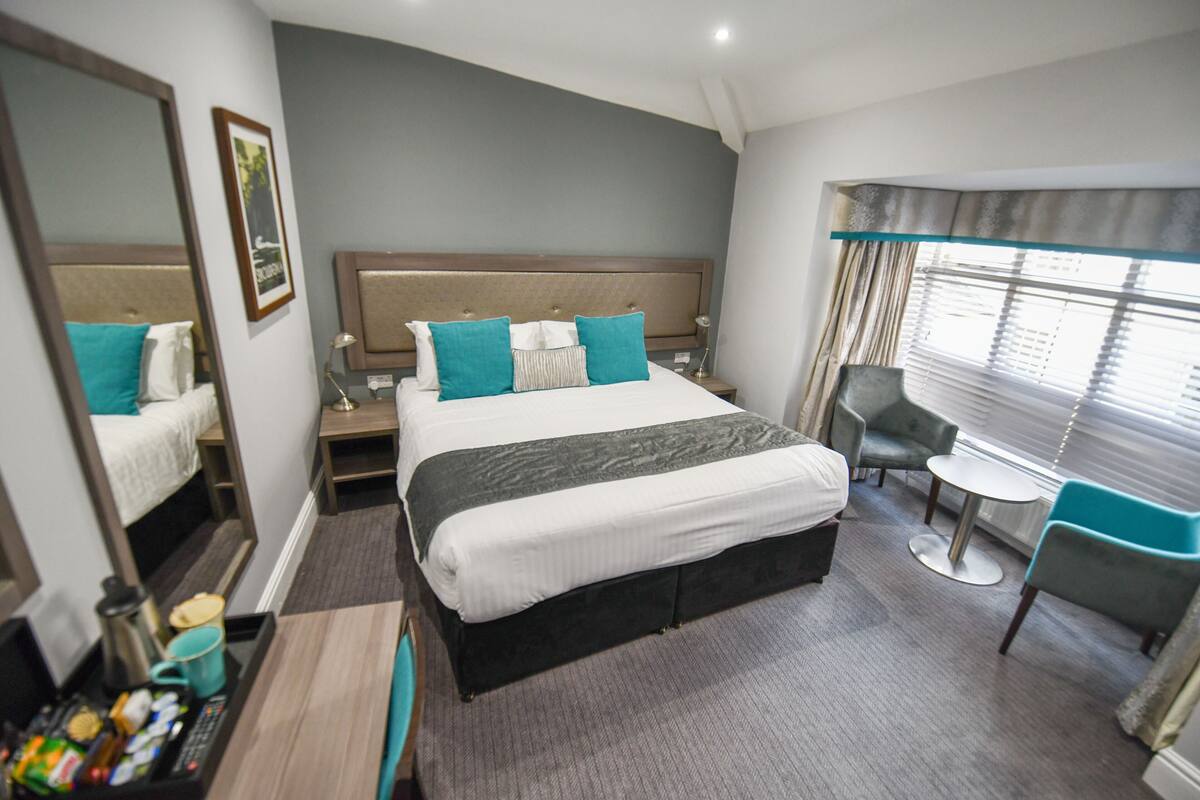 Une chambre d’hôtel avec un grand lit, un bureau avec une chaise, une petite table et une fenêtre avec des rideaux.