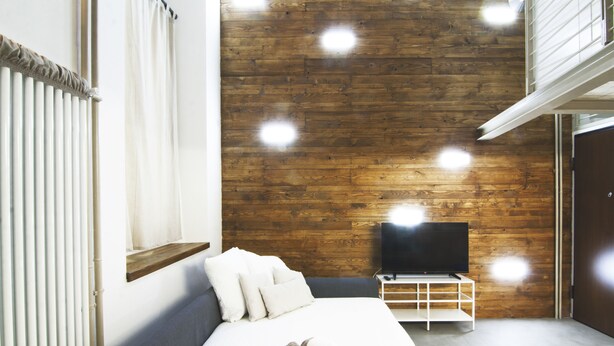 A modern bedroom with a wooden wall, a flat-screen TV, a bed with white linens, and a rolled towel on the bed. - Alessia's Flat - Mac Mahon (Milan)