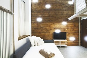 Un dormitorio moderno con una pared de madera, un televisor de pantalla plana, una cama con sábanas blancas y una toalla enrollada sobre la cama.