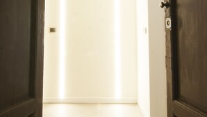 A hallway with a closed door at the end, a light switch on the wall, and a plain white wall. - Alessia's Flat - Mac Mahon (Milan)