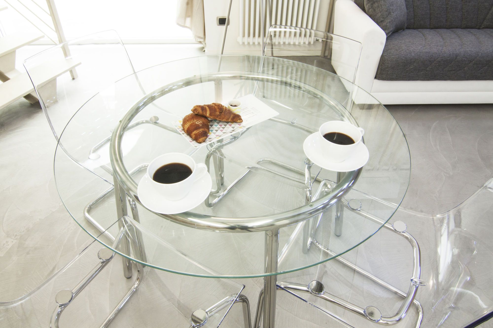 A glass table with two cups of coffee and a plate of croissants.