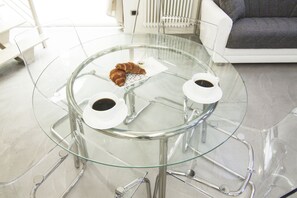 Een glazen tafel met twee koffiekopjes en een bord croissants.