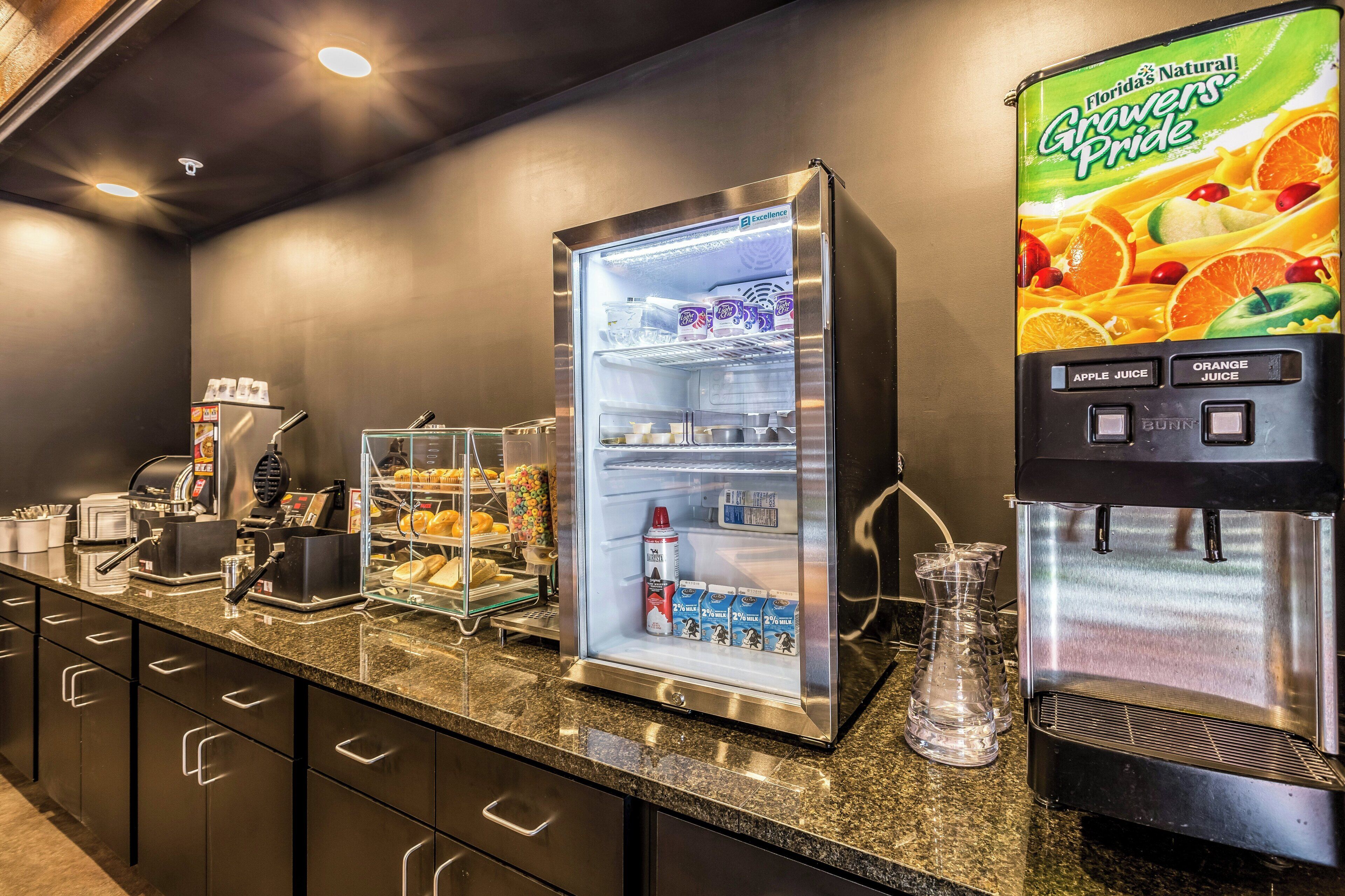 Ein Selbstbedienungs-Frühstücksbereich mit Kühlschrank, Saftspender und Kaffeeautomat.