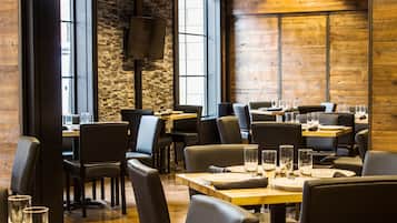 Un restaurante con paredes de madera, detalles de piedra y mobiliario moderno. Las mesas están preparadas con vasos y platos.