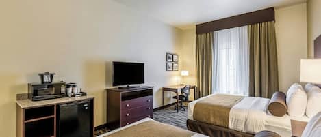 Habitación de hotel con dos camas, televisión, escritorio con silla, kitchenette pequeña y ventana con cortinas.