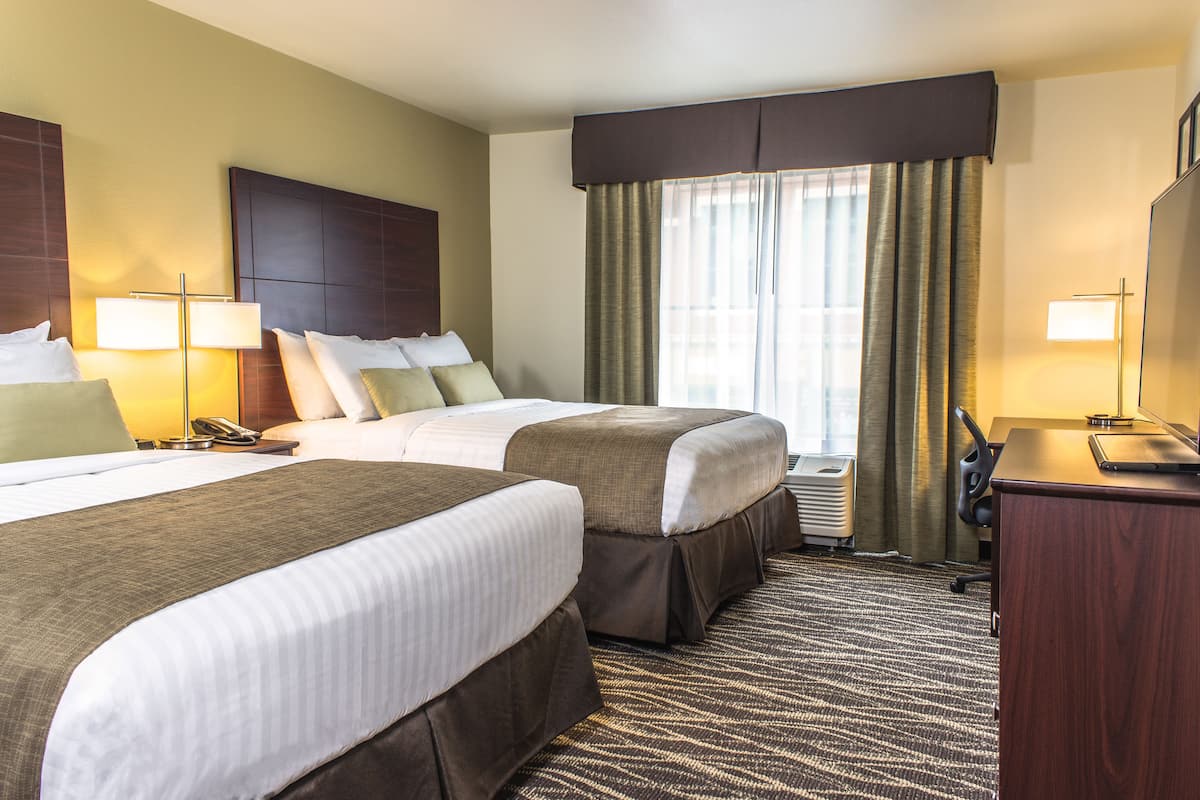 A hotel room with two beds, a desk, a chair, a lamp, a telephone, and a window with curtains.
