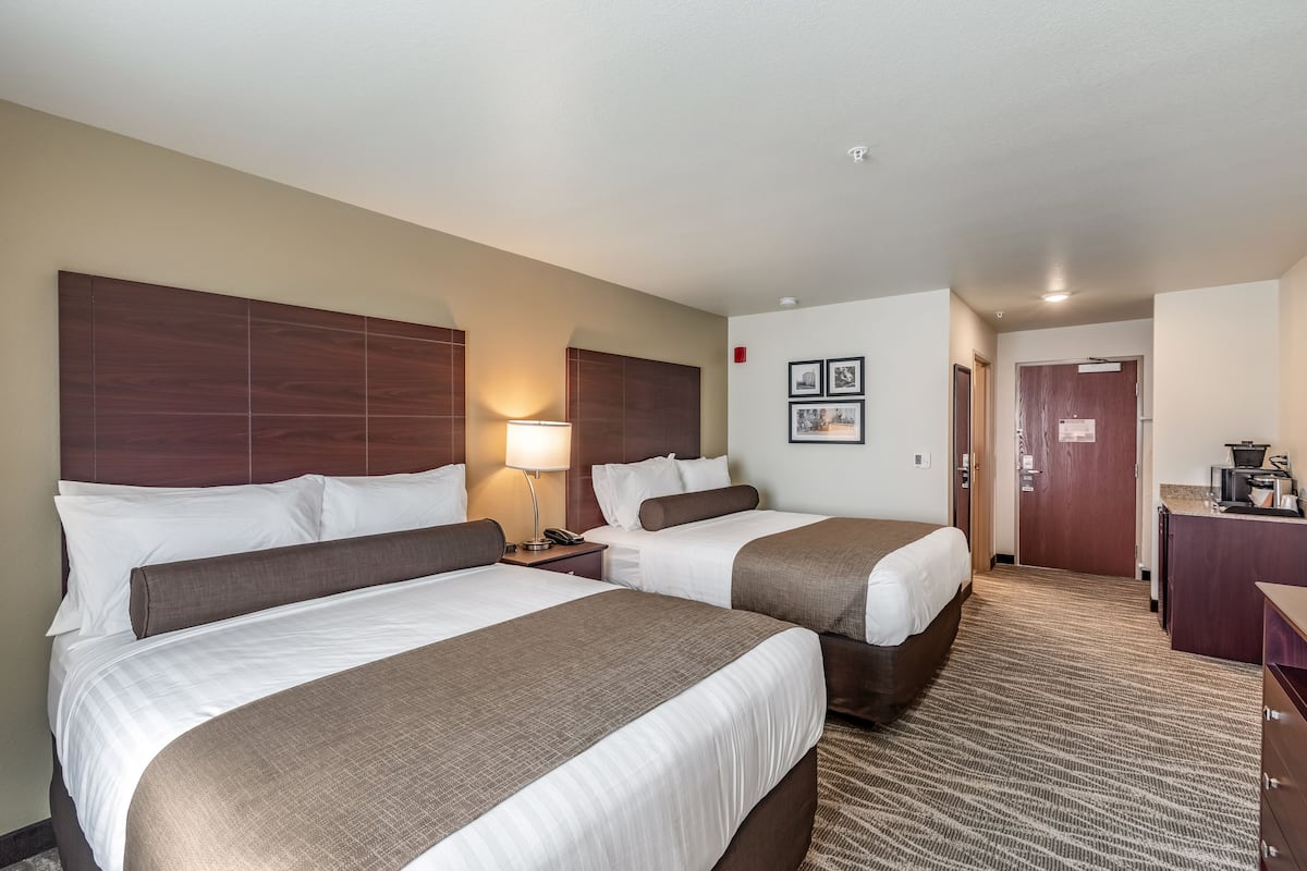 A hotel room with two beds, a desk, a lamp, and a door leading to another room.