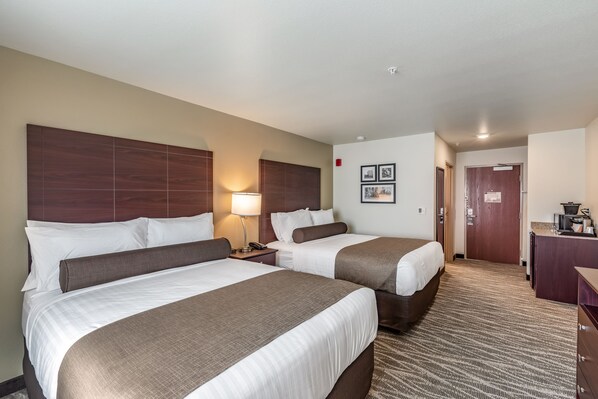 A hotel room with two beds, a desk, a lamp, and a door leading to a bathroom.