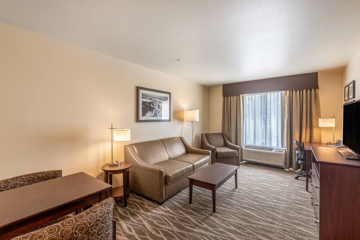 A hotel room with a sofa, armchair, desk, and a large window with curtains.
